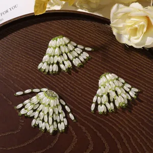 Three fan-shaped ornaments with white rice-shaped beads and green accents on a dark wood tray