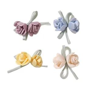Vier Haaraccessoires mit Satinrosen in Rosa, Blau, Gelb und Creme, jeweils mit salbeigrüner Schleife