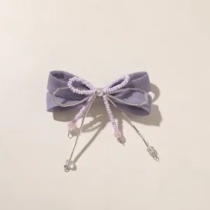 Dettaglio di un fiocco in tessuto color lavanda con perline, fili argentati e ciondoli rosa