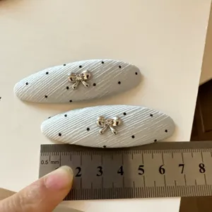 Dos pinzas de tela azul claro acanalada, con puntos negros y lazos plateados junto a una regla