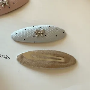 Primer plano de una pinza celeste con lunares y lazo metálico, junto a su reverso de ante.