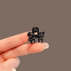 Close-up of a small black bow-shaped claw clip with sparkling dark stones, held between fingers