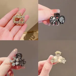 Four small jeweled metal hair clips shown in hand, featuring a square design and floral accents