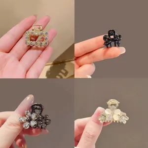 Four jeweled mini hair clips shown in hand, with gold and black floral, bow, and square designs