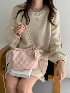 Detail of a pink quilted bag with silver chain strap and pearl charm, held by a seated model