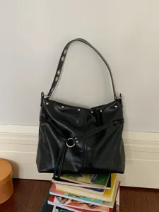 Borsa nera in similpelle con borchie argentate e dettaglio ad anello, appesa sopra alcuni libri