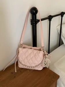 Pink quilted flap bag with a chain-trimmed edge and pearl heart charm, displayed on a wooden table