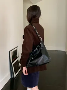 Vista posteriore di una persona con borsa nera in similpelle e anelli argentati, in un interno