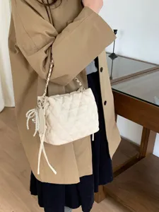 Cream quilted bag worn over a coat, with a chain strap, drawstring ties and pearl charm.