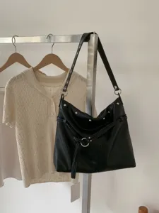Dettaglio della borsa nera in similpelle con borchie argentate, anello metallico, laccio e nappa