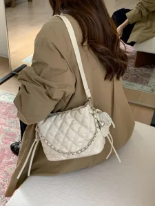Side view of an ivory quilted bag worn crossbody, with a silver chain and pearl heart charm