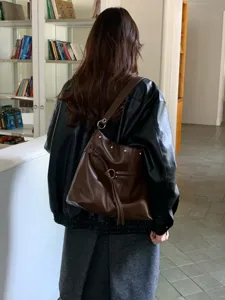 Vista da dietro di una modella con borsa marrone in similpelle, borchie e anello metallico