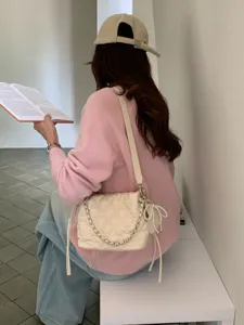 Lifestyle view of a woman wearing a cream quilted shoulder bag with a chain strap and pearl bow