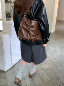 Vista posteriore di una modella con borsa in similpelle marrone, anelli e borchie metallici