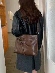 Vista posteriore di una borsa marrone in similpelle con borchie e tracolla regolabile, al chiuso