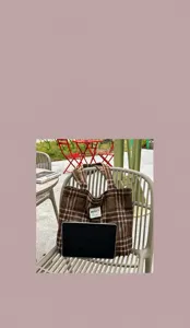 Plaid wool tote resting on an outdoor chair with a tablet tucked inside, shown in a lifestyle scene