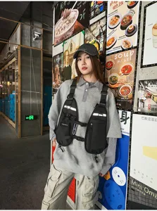 Model wearing a black chest vest bag with front pockets, reflective strips and adjustable straps