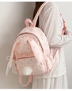 Un modèle porte un sac rose à pois, avec des oreilles de lapin et un pompon doux en décoration