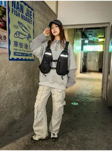 Model wearing a black chest vest with front pockets and adjustable straps in an urban hallway