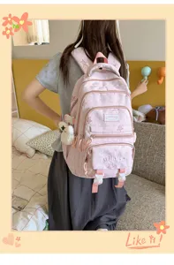 Vue de dos d'une élève portant un sac à dos rose à poches zippées, avec un petit ours blanc accroché