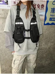 Black chest bag worn over a sweatshirt, with reflective strips, zip pockets and adjustable buckles