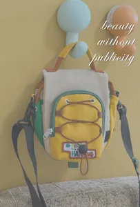 Sac multicolore suspendu au mur, avec poche avant, cordons jaunes et bandoulière réglable visible