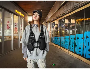Street-style view of a black nylon chest bag with silver reflective strips worn over a gray hoodie