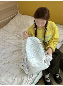 Une personne montre un sac bleu clair à carreaux, avec panneau blanc à pois et breloques en peluche