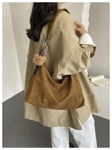 Détail d’un sac bandoulière marron en suédine porté avec un manteau beige et un petit ours
