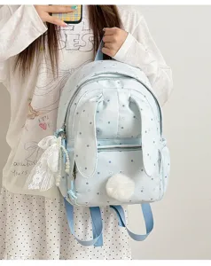 Sac à dos bleu clair porté par un modèle, à pois, avec oreilles de lapin et pompon doux