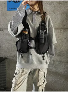 Model wearing a black multi-pocket chest bag with adjustable straps against a concrete wall