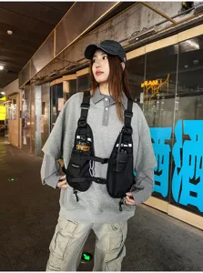 Black tactical chest rig with adjustable straps, worn over a gray hoodie in a street setting
