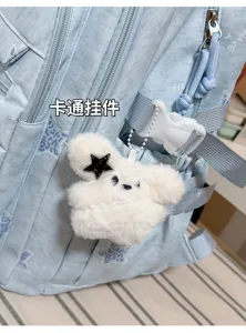 Gros plan sur un porte-clés ours blanc duveteux, avec étoile noire et perles, sur un sac à dos bleu