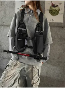 Black chest bag worn over a gray sweatshirt, showing adjustable straps, buckles and reflective trim