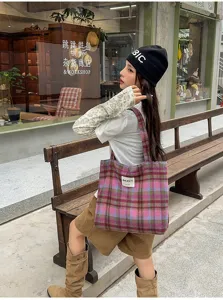 Street-style view of a woman carrying a pink and purple plaid tote beside a wooden bench