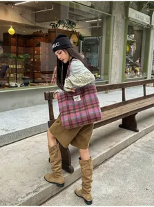Street-style photo of a model holding a pink-purple plaid tote beside a wooden bench