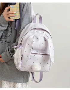 Un modèle porte un sac à dos lavande à pois, avec oreilles de lapin, pompon et breloques en dentelle.