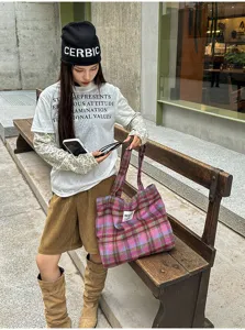 Street-style view of a pink-purple plaid fabric bag with twin handles and a small front label