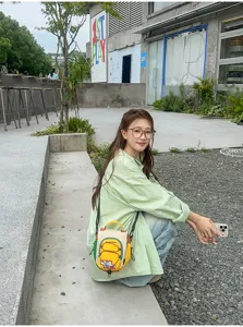 Vue de rue : un modèle assis porte un petit sac jaune et crème à cordon avec bandoulière réglable