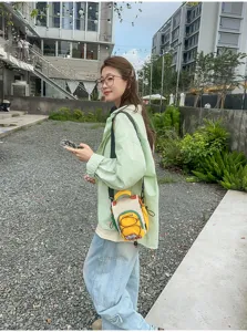 Dans la rue, une femme porte un sac bandoulière crème, jaune et vert avec poche zippée à l’avant