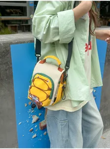 Vue de côté d'un petit sac jaune et crème porté en bandoulière, avec cordon frontal et bordure verte