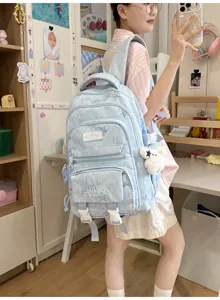 Élève portant un sac à dos bleu clair effet denim, avec poches zippées et un petit porte-clés ours