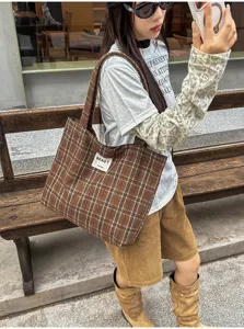 Woman carrying a brown plaid tote over her shoulder beside a wooden bench, BEAUT label visible