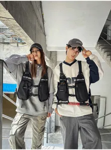 Two models wear black multi-pocket chest packs with adjustable straps in an urban stairwell
