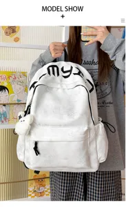 Sac à dos blanc porté par un modèle, avec étoiles en relief, lettres noires et breloque en peluche.