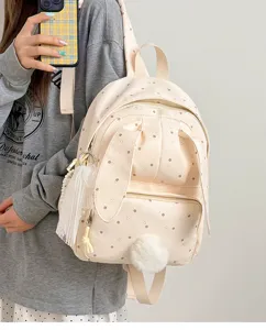 Gros plan sur un sac à dos crème à pois et cœurs, avec pompon et pampille, porté par un modèle