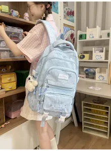 Vue portée d’un sac bleu clair à étoiles, avec plusieurs poches et un pendentif ours en peluche blanc