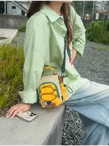 Vue extérieure d'un petit sac bandoulière jaune, bordure verte et poche avant porté par un modèle