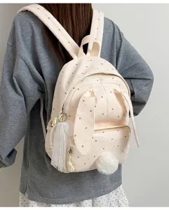 Sac à dos crème à pois bruns, avec oreilles de lapin et pampilles, porté sur le dos d’une personne