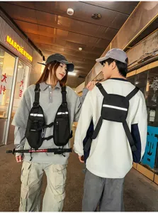 Two models wear black nylon chest bags with adjustable straps and reflective trim in a corridor